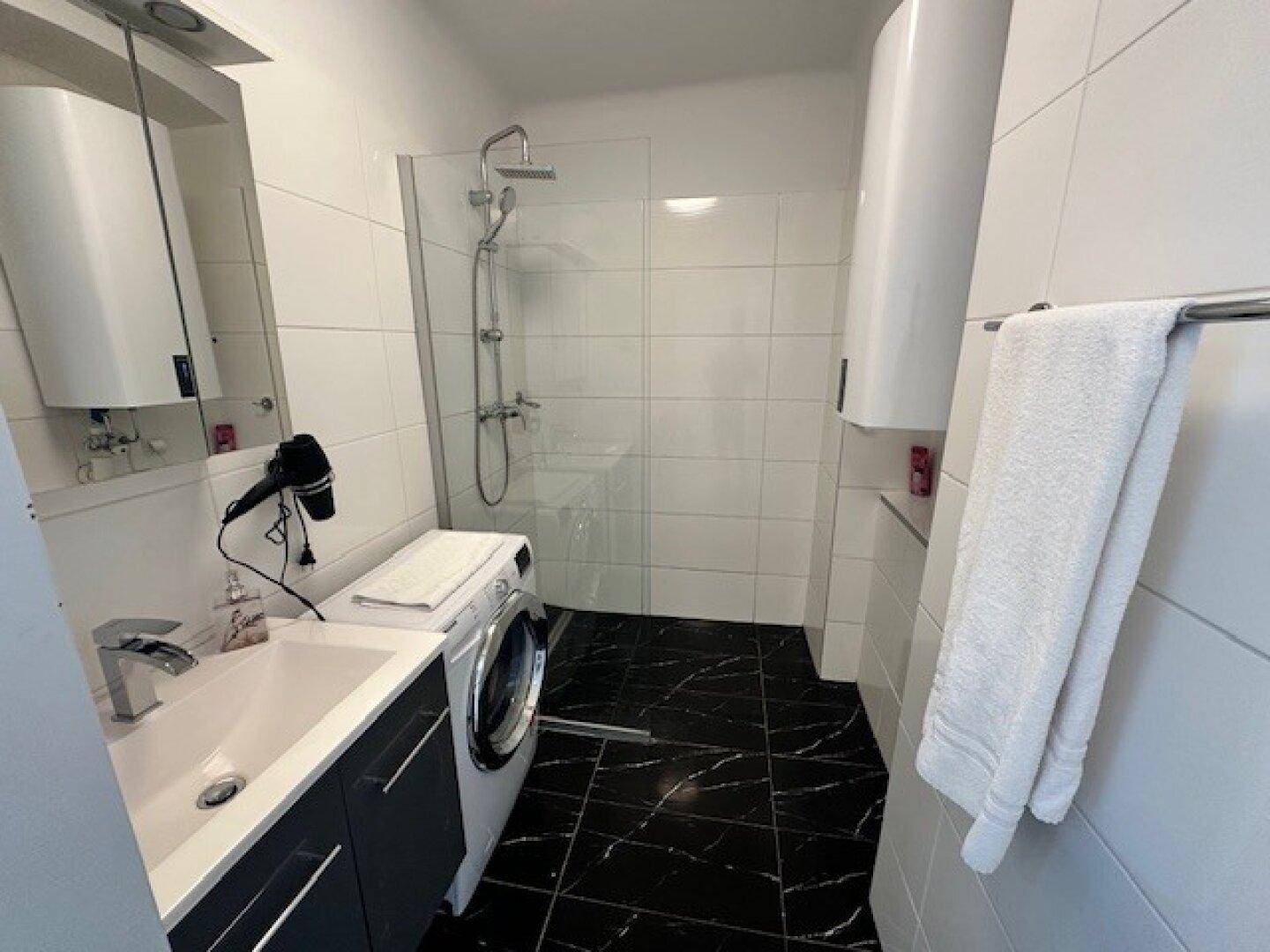 Helles Badezimmer mit Waschbecken, Dusche und Waschmaschine, modern gefliest.