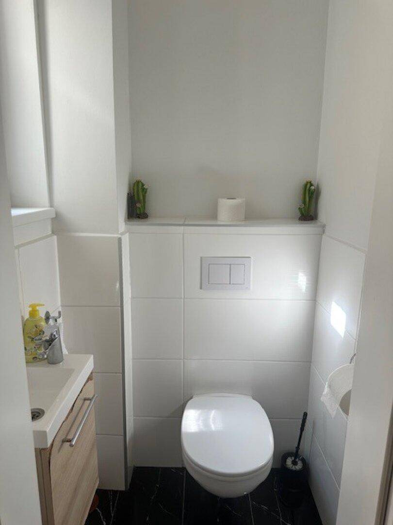 Kleines Gäste-WC mit Wand-WC und minimalistischem Waschbecken, hell gefliest.