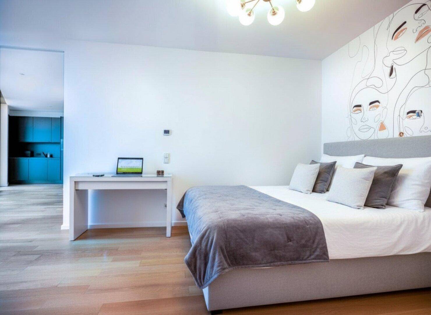 Helles Schlafzimmer mit Doppelbett, Schreibtisch und moderner Wanddekoration.