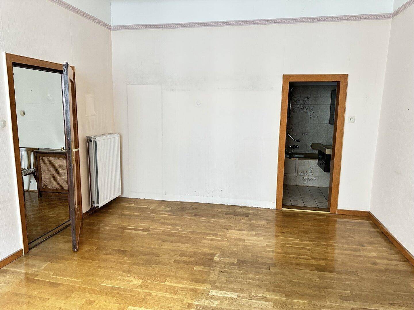 Geräumiges Zimmer mit Parkettboden und Zugang zu weiteren Räumen, inklusive Heizkörper.