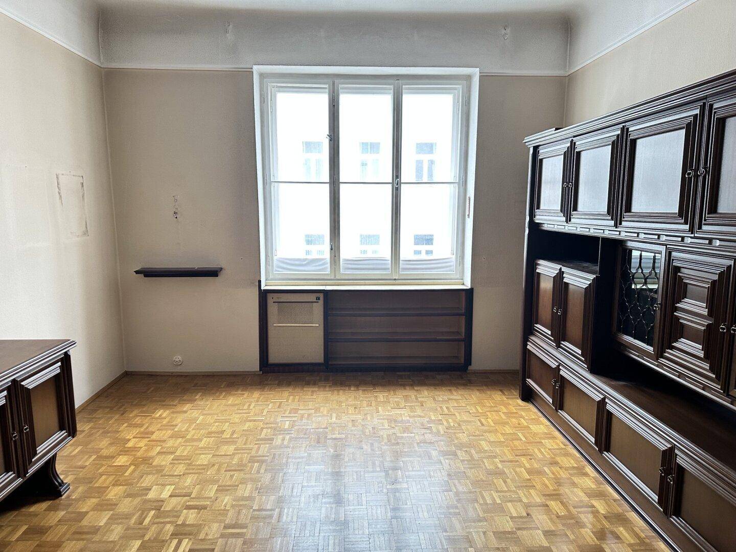 Wohnzimmer mit Parkettboden, großem Fenster und traditionellen dunklen Holzmöbeln.