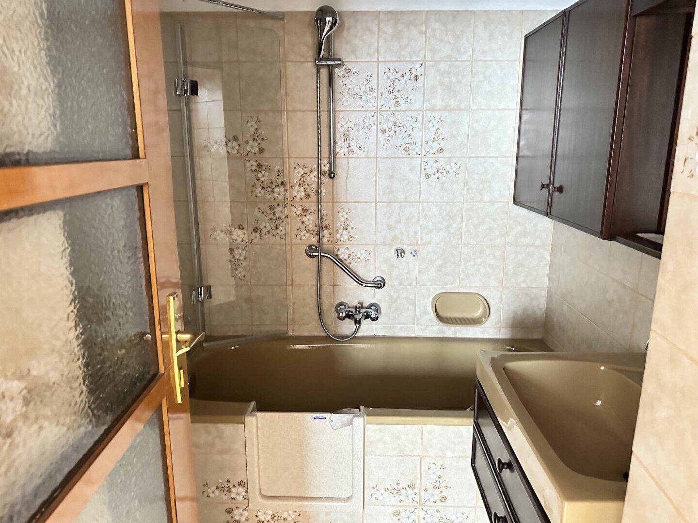 Badezimmer mit Badewanne, Dusche und beigefarbenen Fliesen im älteren Stil.