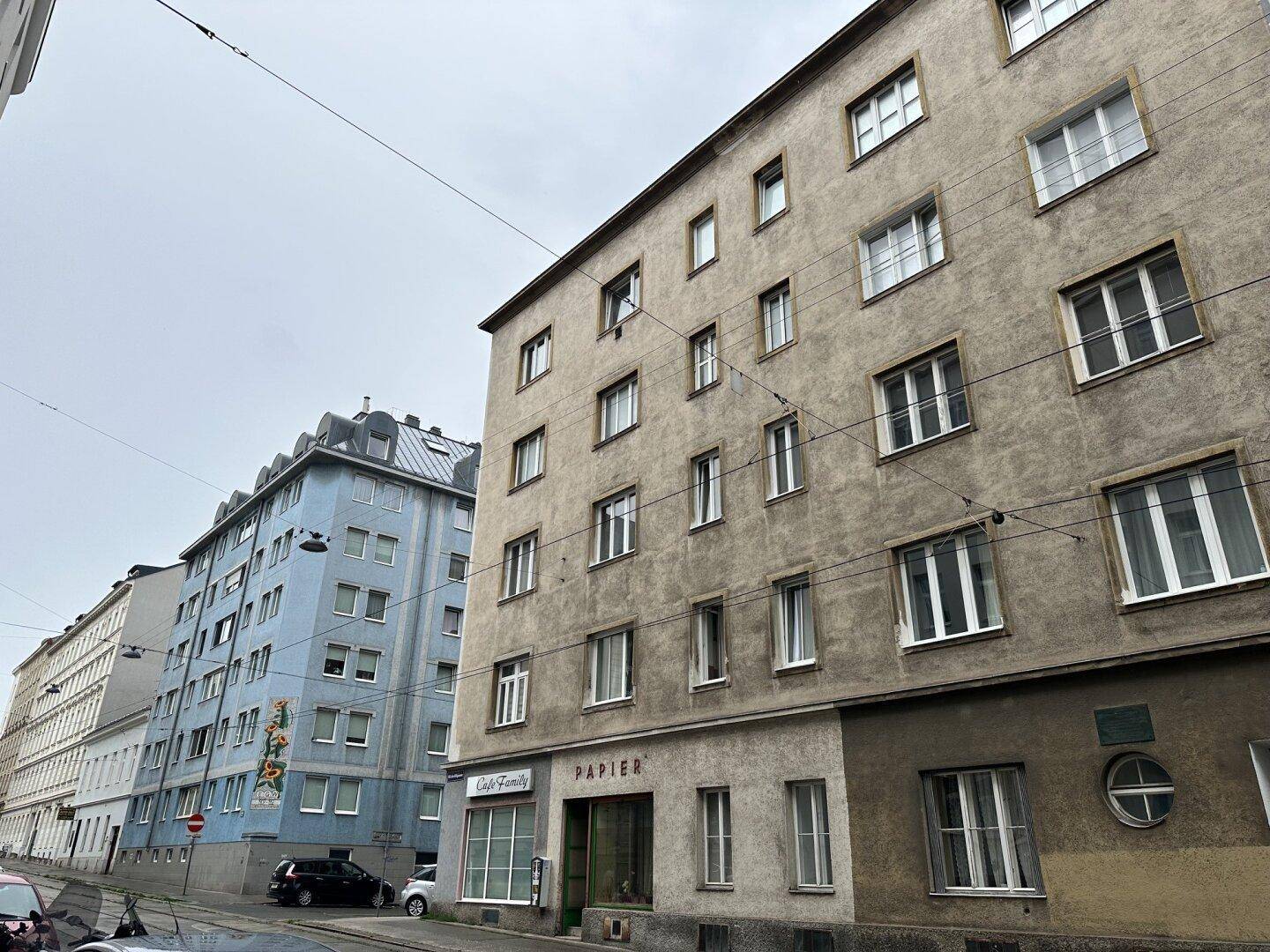 Fassade eines älteren Mehrfamilienhauses an einer Stadtstraße mit vielen Fenstern.