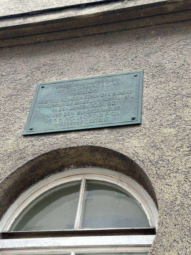 Historische Gedenktafel an der Fassade eines Gebäudes über einem Fenster.