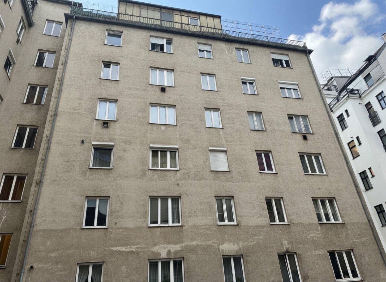 Fassade eines Mehrfamilienhauses mit vielen Fenstern unter einem blauen Himmel.