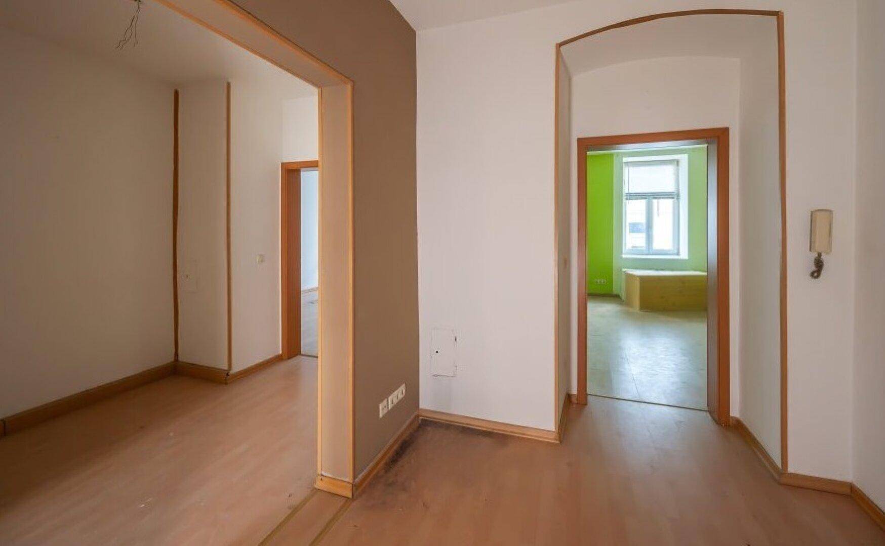 Flur mit Holzböden und Durchgängen zu weiteren Räumen, einer davon mit grünen Wänden.