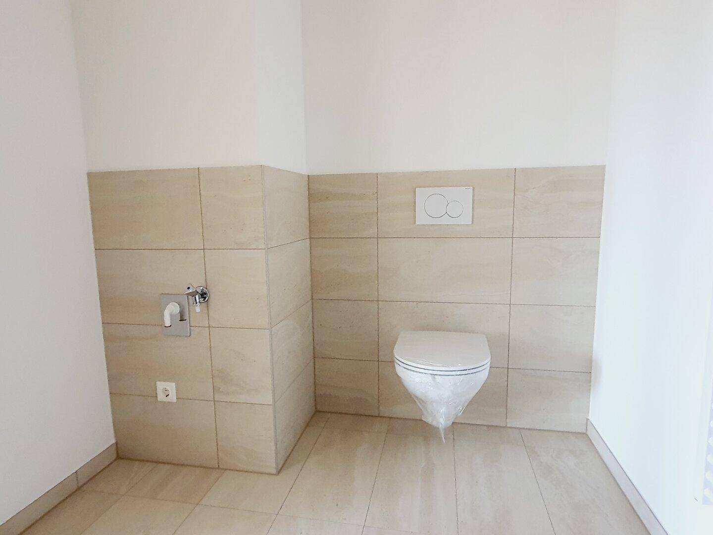 Modernes WC mit beigefarbenen Fliesen und wandhängender Toilette, in neuwertigem Zustand.