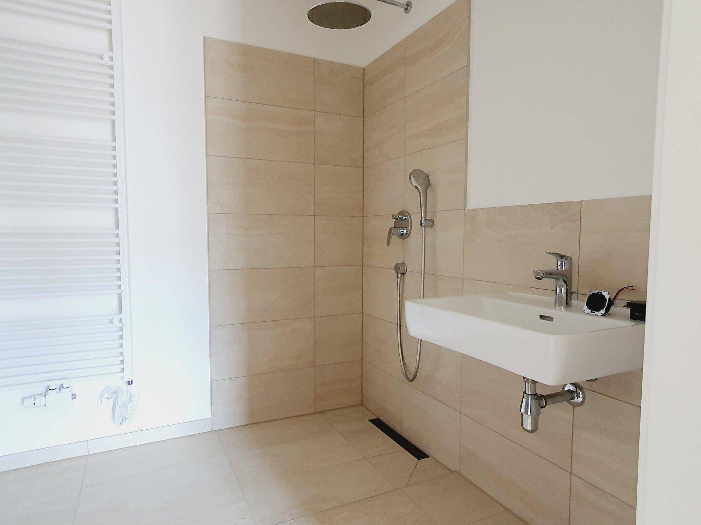 Modernes Badezimmer mit beigefarbenen Fliesen, ebenerdiger Dusche und beheiztem Handtuchhalter.
