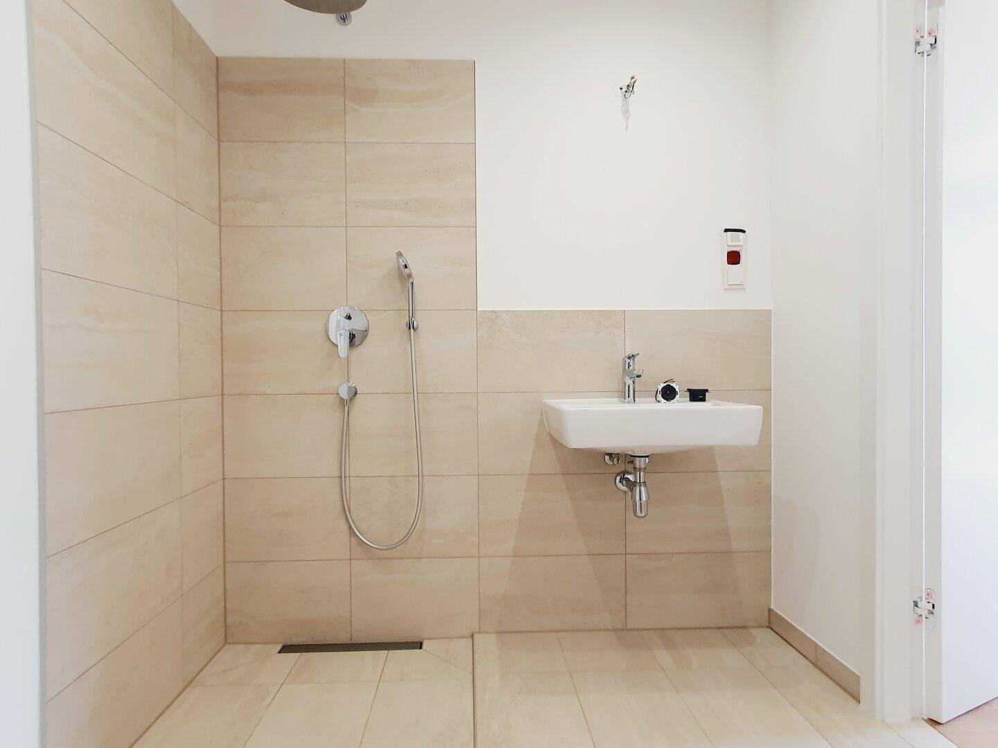 Helles Badezimmer mit beigefarbenen Fliesen, ebenerdiger Dusche und modernem Waschbecken.