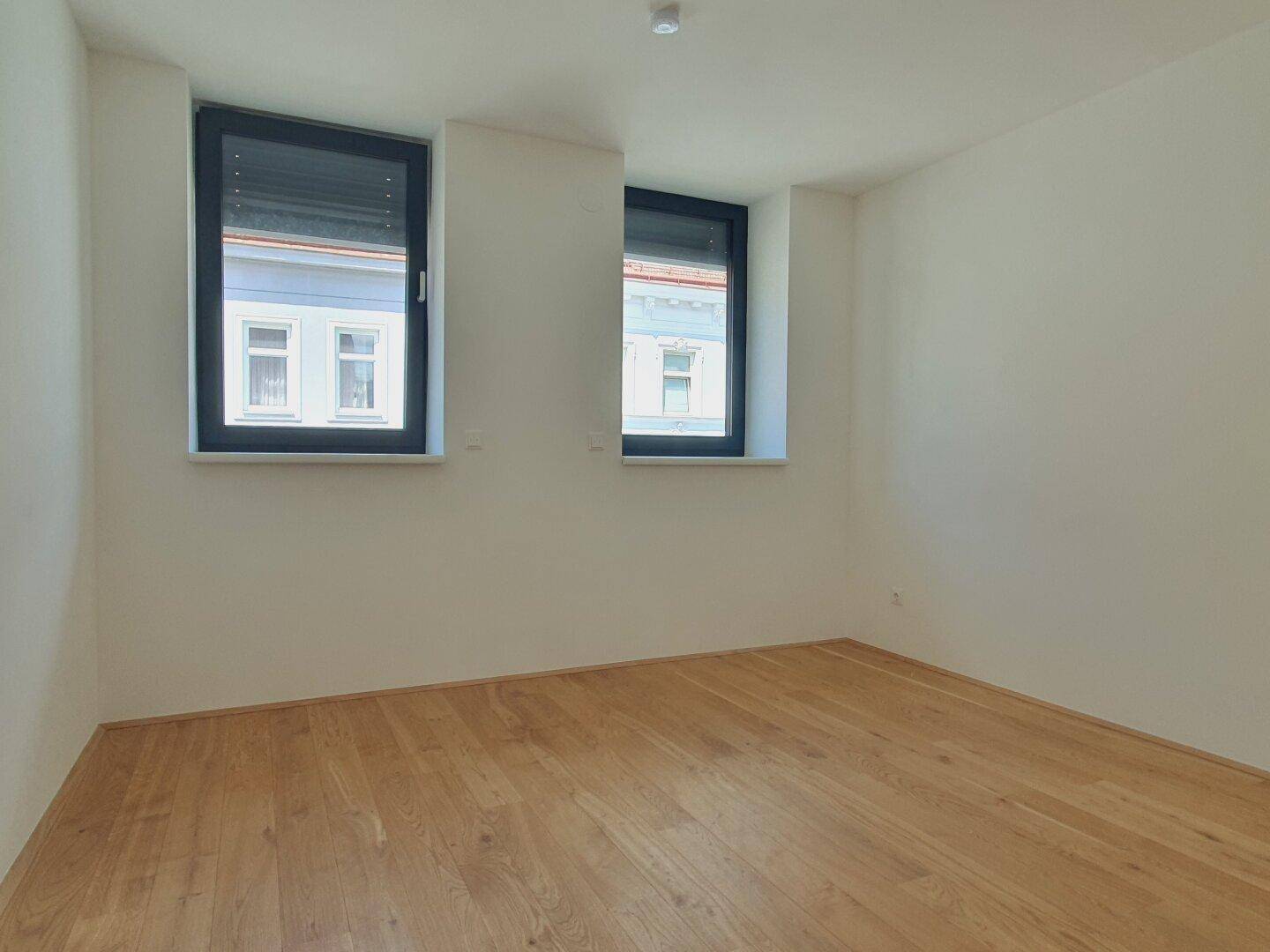 Geräumiges Schlafzimmer mit Holzboden und zwei Fenstern, die viel Tageslicht hereinlassen.