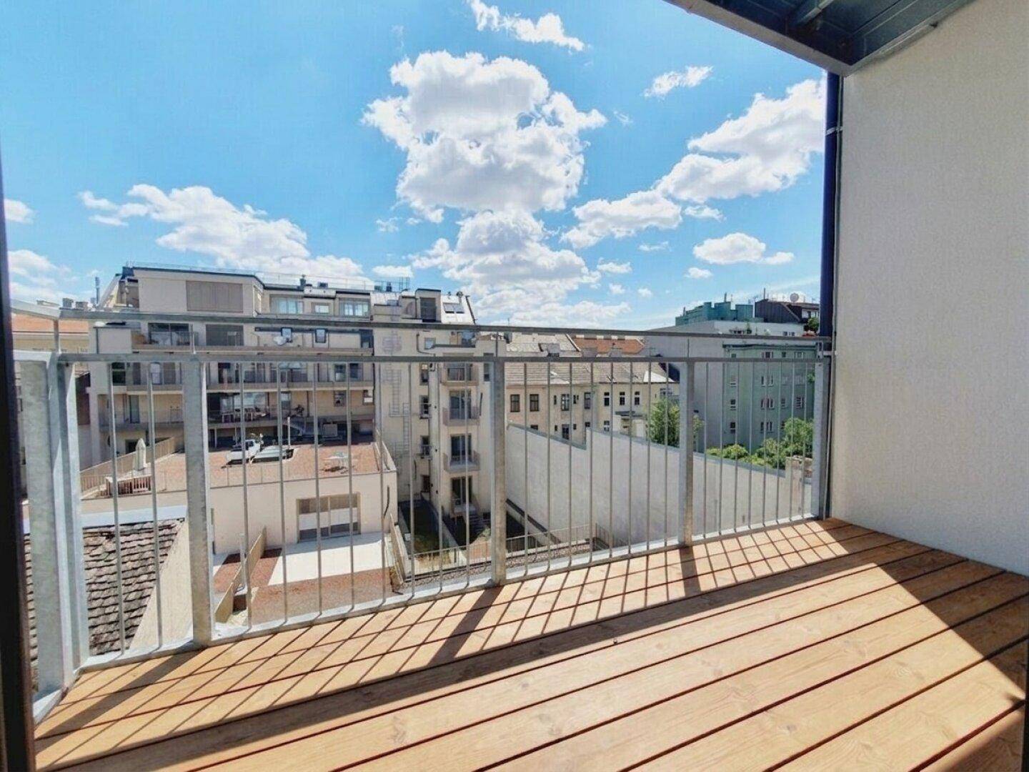 Heller Balkon mit Holzbelag und Metallgeländer, bietet einen weiten Blick über die Stadt.