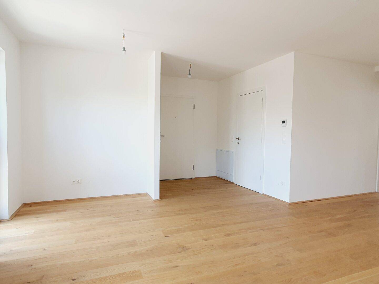 Heller, leerer Raum mit Holzboden und zwei Türen, der verschiedene Bereiche des Apartments verbindet.