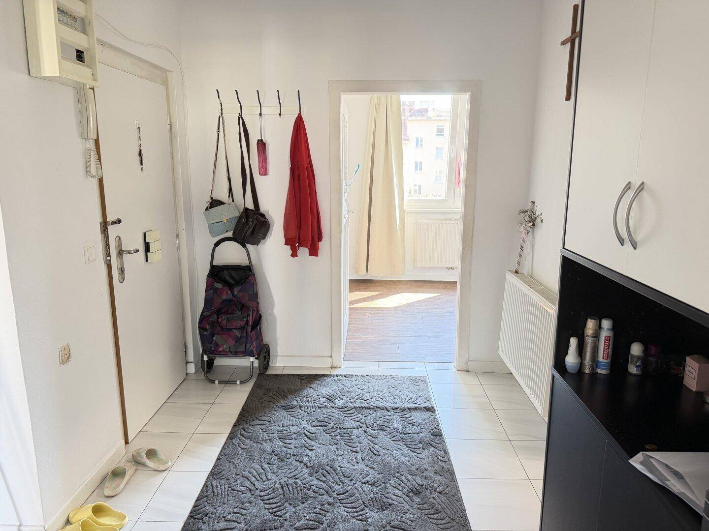 Heller Flur mit weißem Fliesenboden, Garderobe und Zugang zu weiteren Räumen.