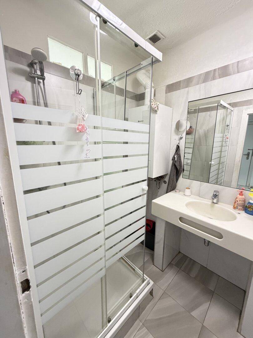 Badezimmer mit Duschkabine, Einzelwaschbecken und Spiegelschrank, hell gefliest.