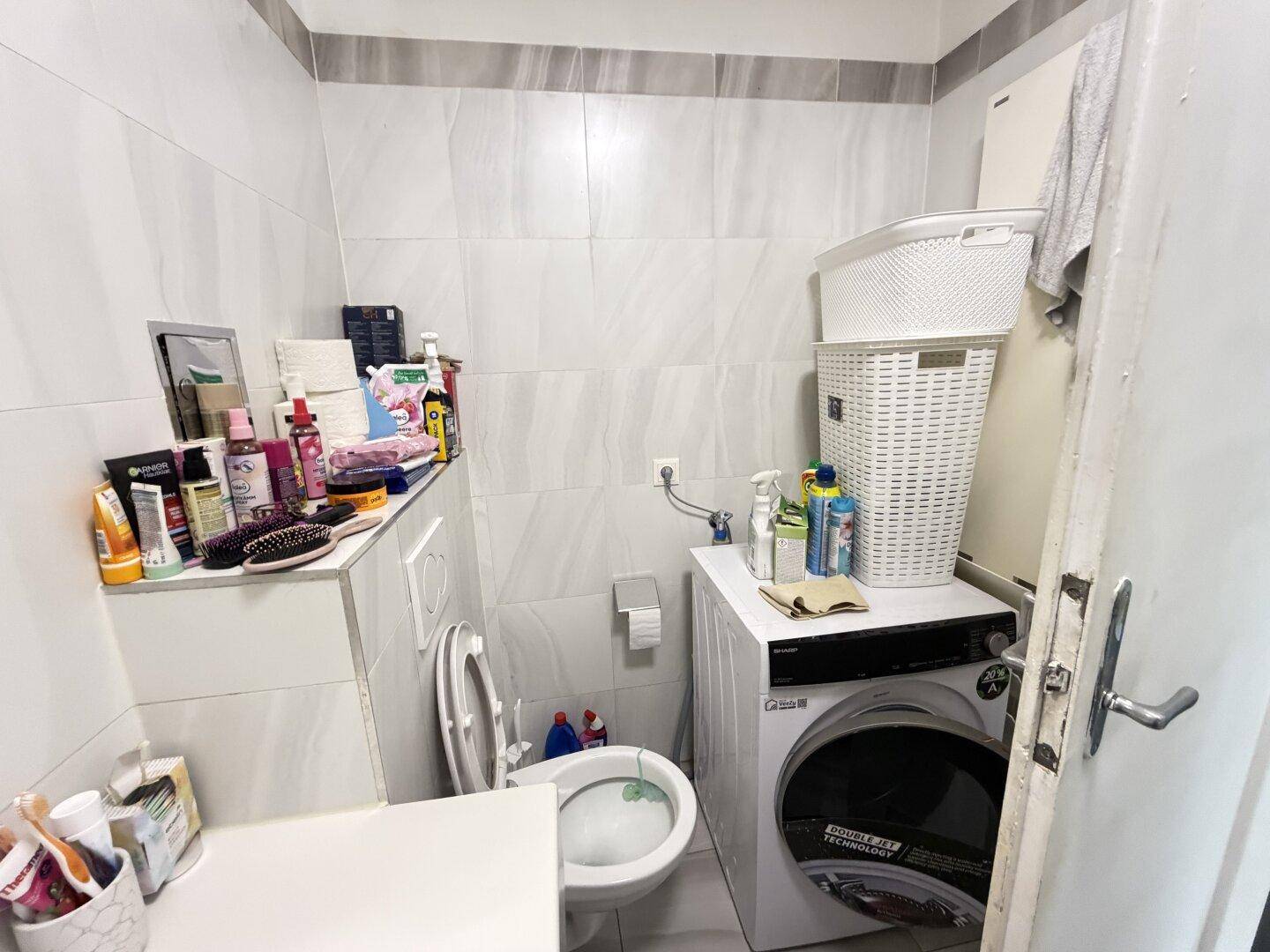 Separates WC mit Waschmaschine und Fliesenboden, praktisch und funktional eingerichtet.
