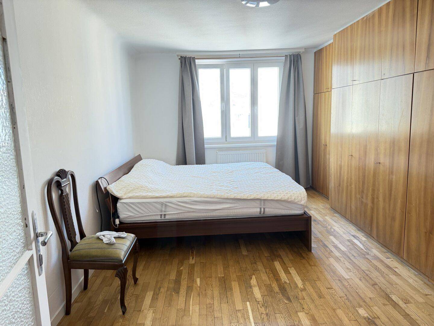 Schlafzimmer mit Holzbett, großem Einbauschrank und Parkettboden, bietet viel Stauraum.