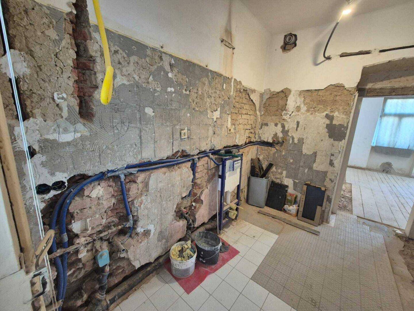 Renovierungsbedürftiges Badezimmer mit sichtbaren Wasserleitungen und Ziegelwerk, bietet Raum für Neugestaltung.