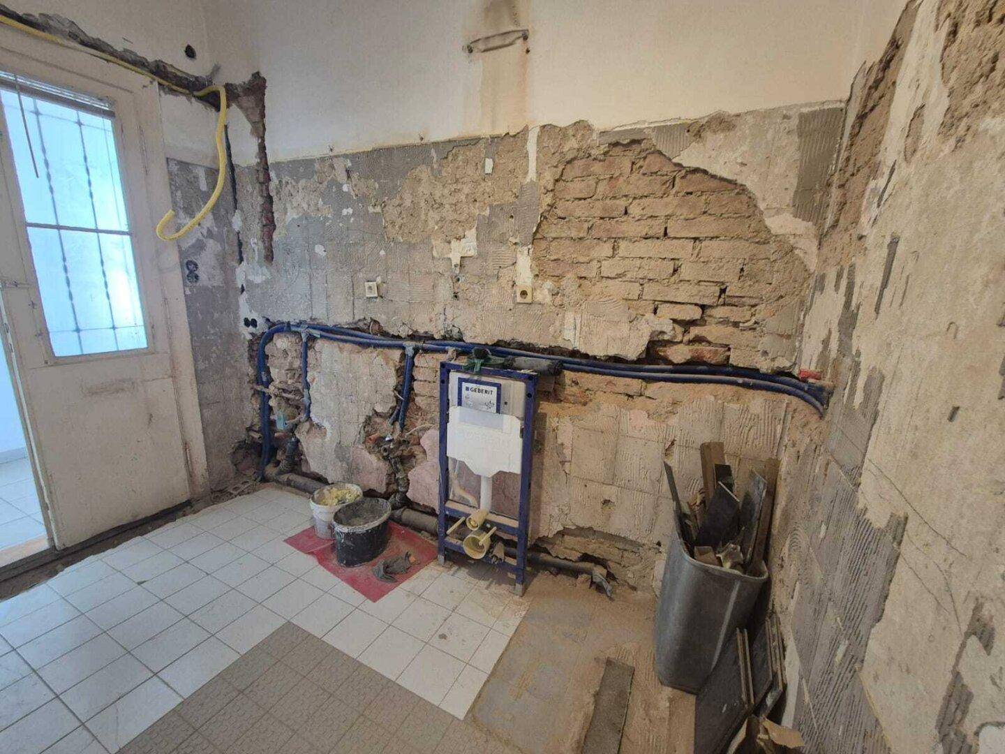Badezimmer im Rohbau mit sichtbaren Installationen und Fliesenboden, bereit für die moderne Ausstattung.