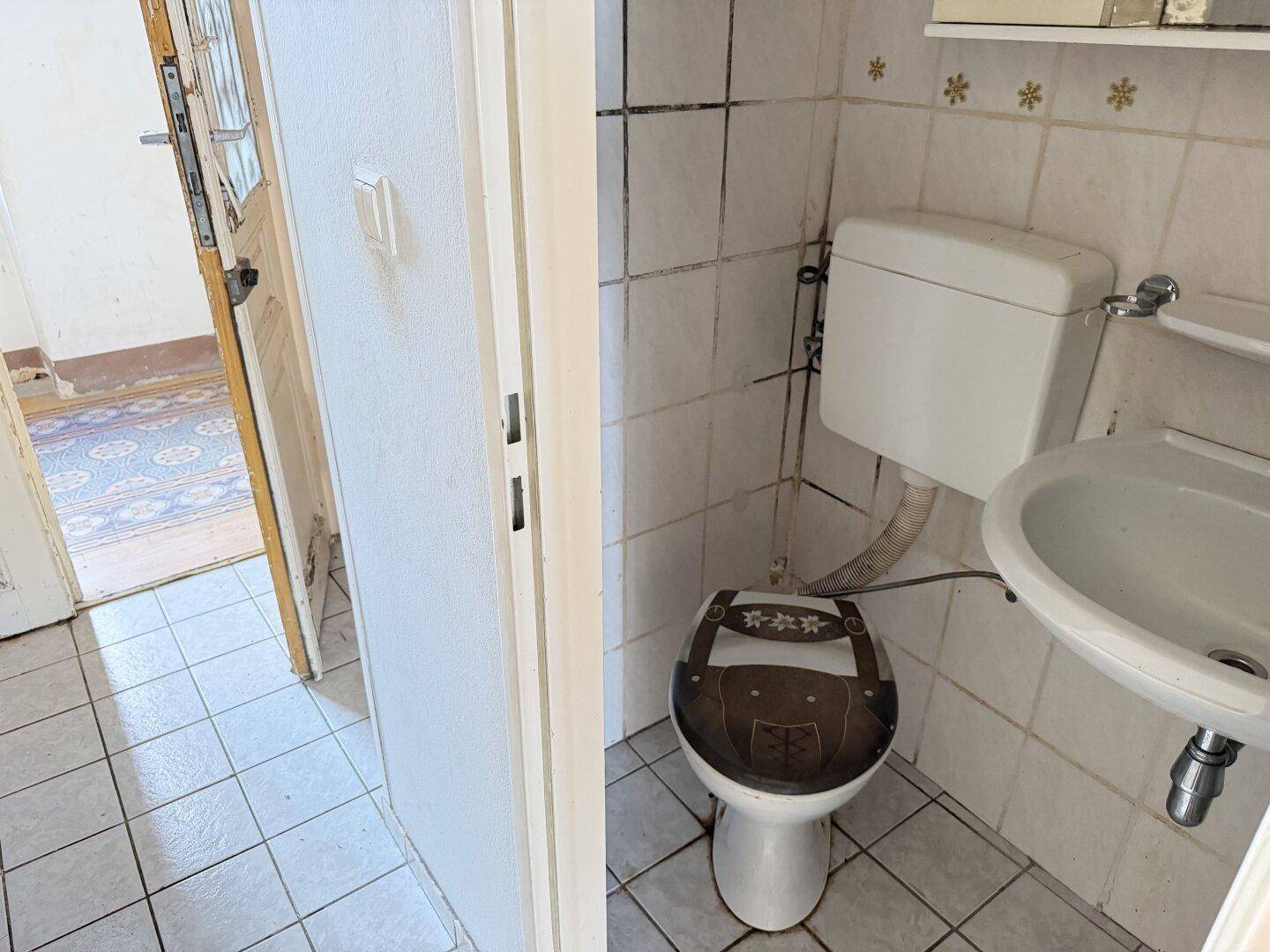Kleines WC mit Fliesenboden und Wandfliesen, ausgestattet mit Toilette und Waschbecken.