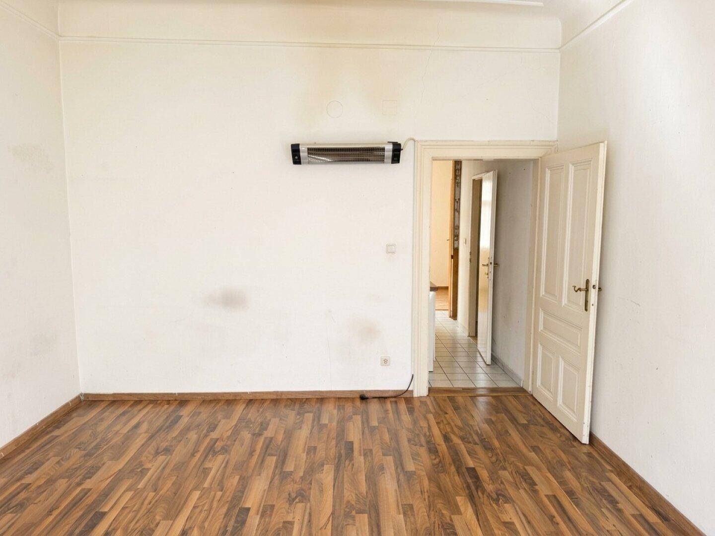 Geräumiges Zimmer mit Laminatboden und Infrarotheizung, das zu weiteren Räumen führt.