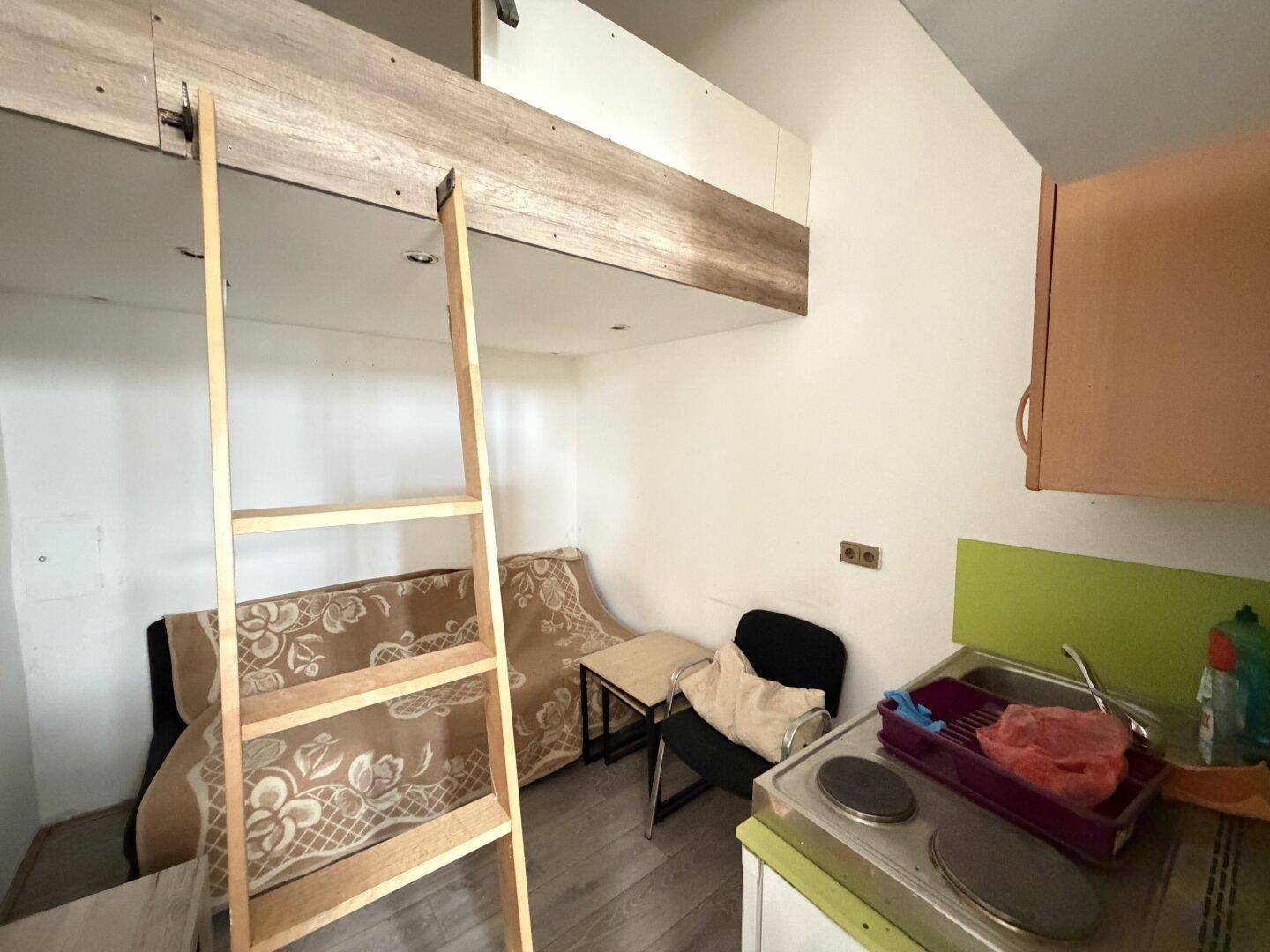 Kompakter Wohnbereich mit Schlafempore, kleiner Küchenzeile und Sofa, ideal für ein Studio-Apartment.