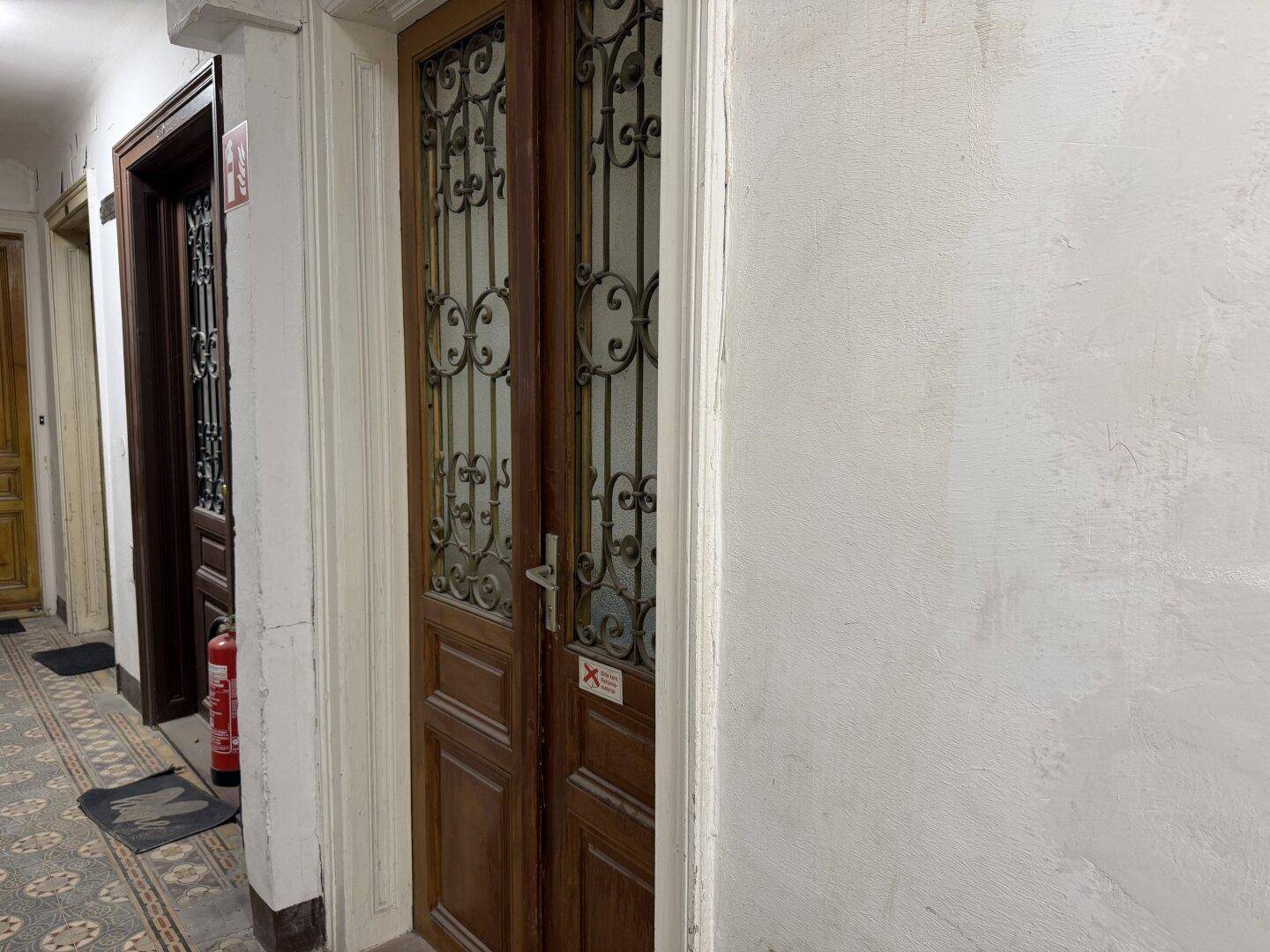 Flur in einem Altbau mit gemustertem Boden und verzierten Holztüren, die zu Wohnungen führen.
