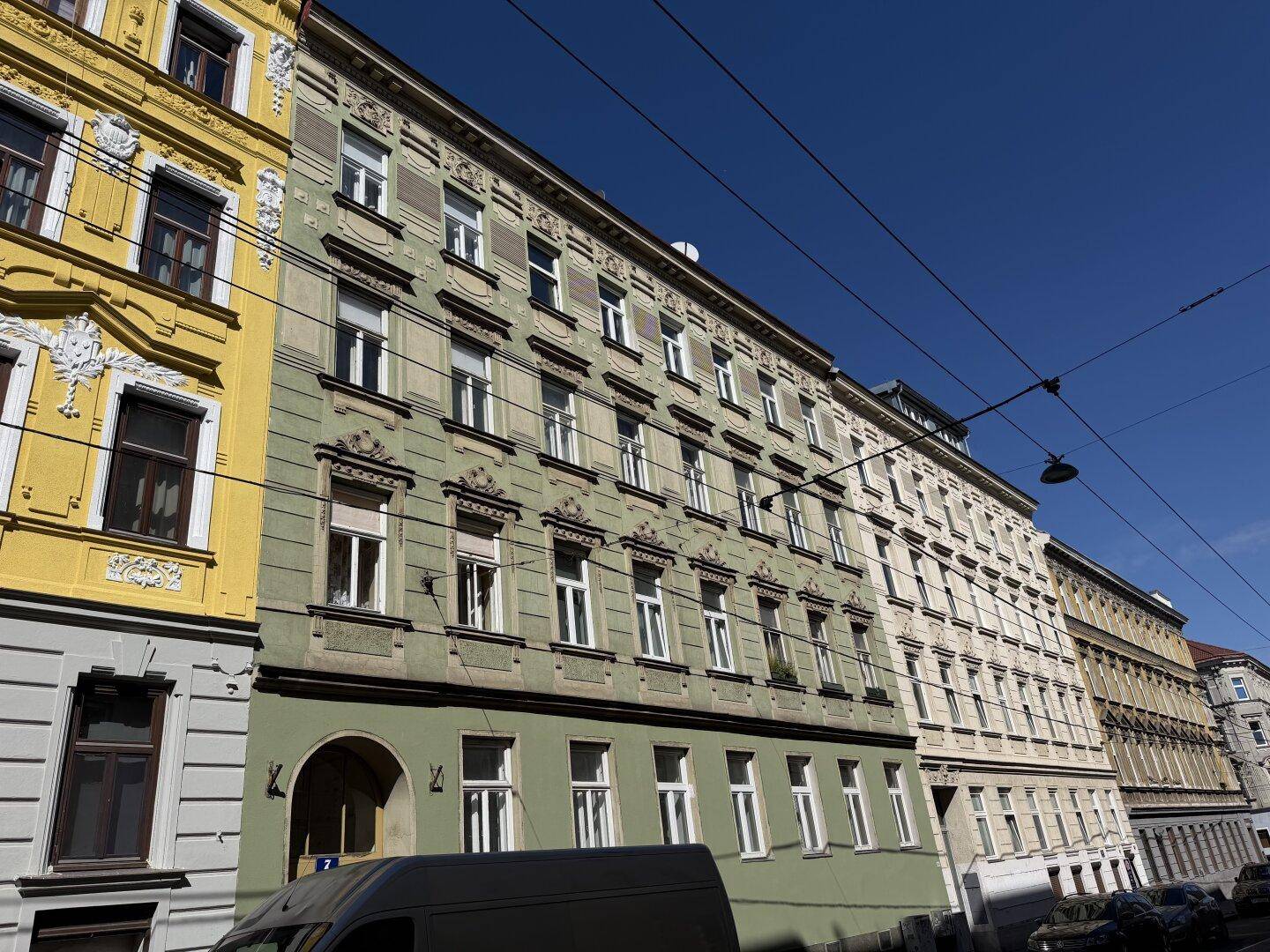 Historisches Mehrfamilienhaus mit grüner Fassade und vielen Fenstern an einem sonnigen Tag.