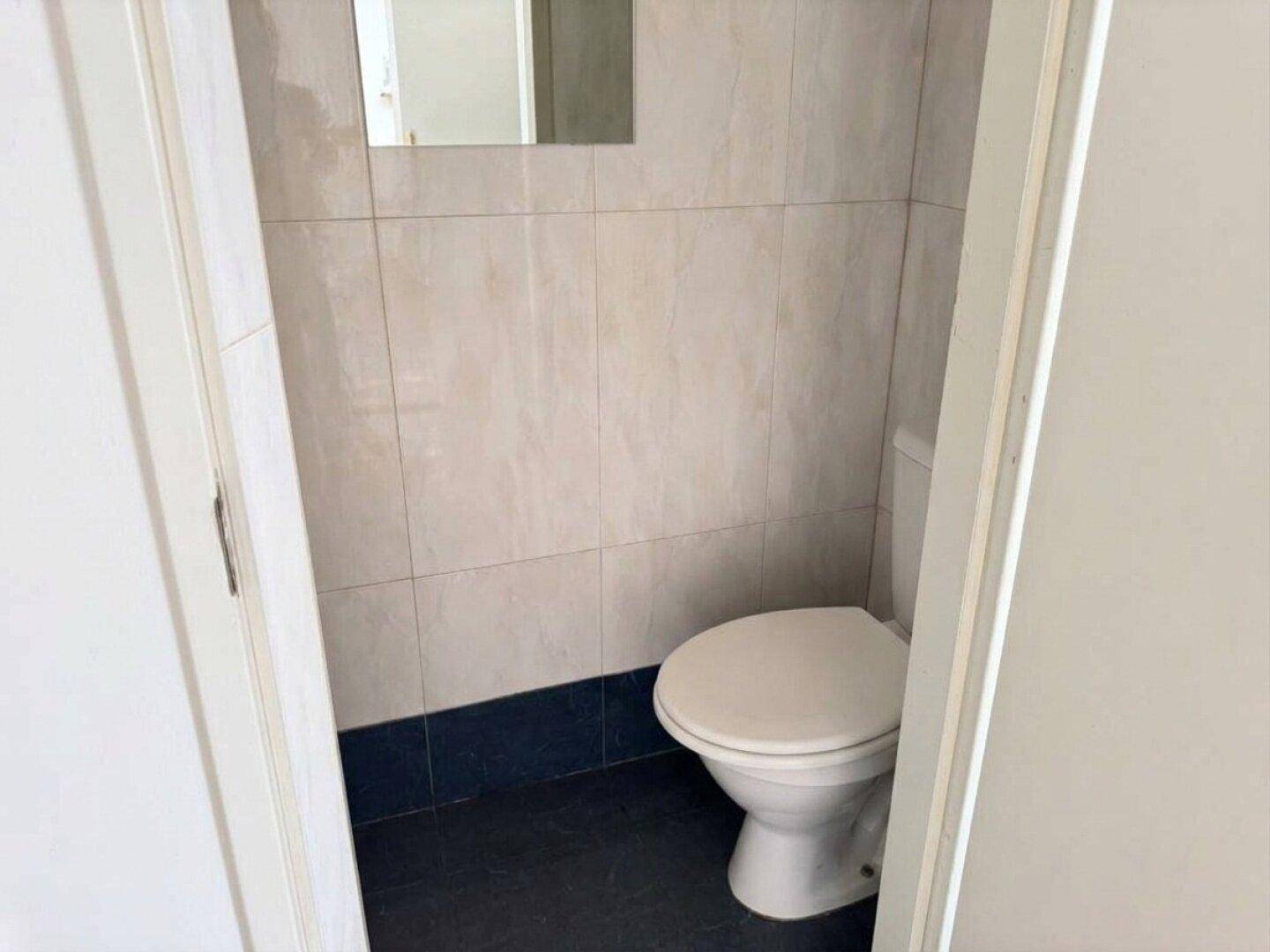 Modernisiertes Gäste-WC mit hellen Wandfliesen und dunklem Boden, sauber und funktional.