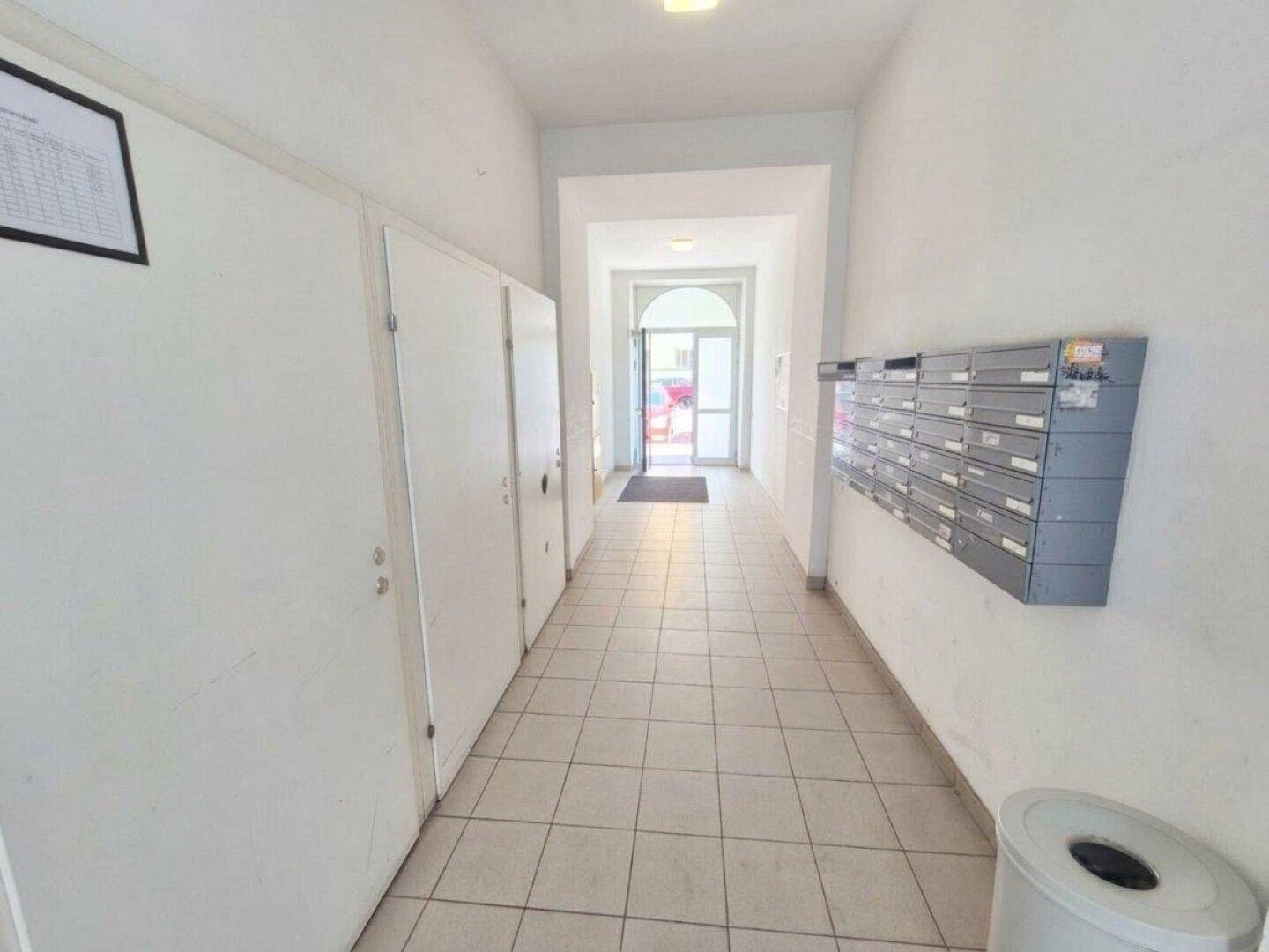 Heller Eingangsbereich mit Fliesenboden, Briefkästen und Abstellkammern, führt zum Gebäudeinneren.