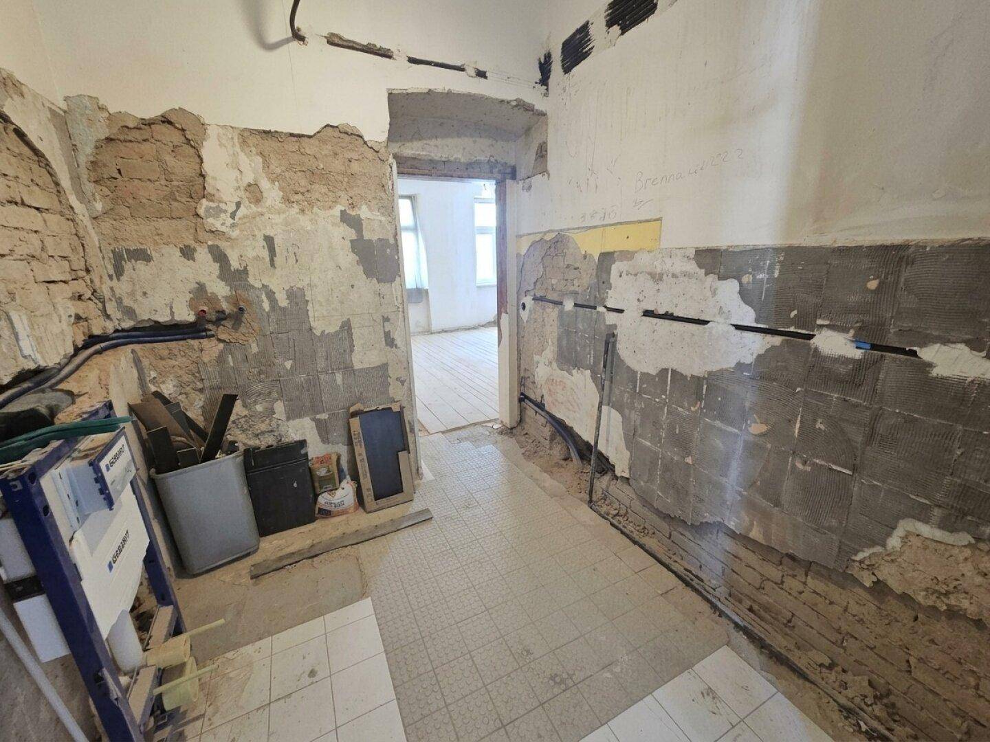 Badezimmer im Rohbau mit freiliegenden Ziegelwänden, Installationen und Fliesenboden, bereit für den Ausbau.