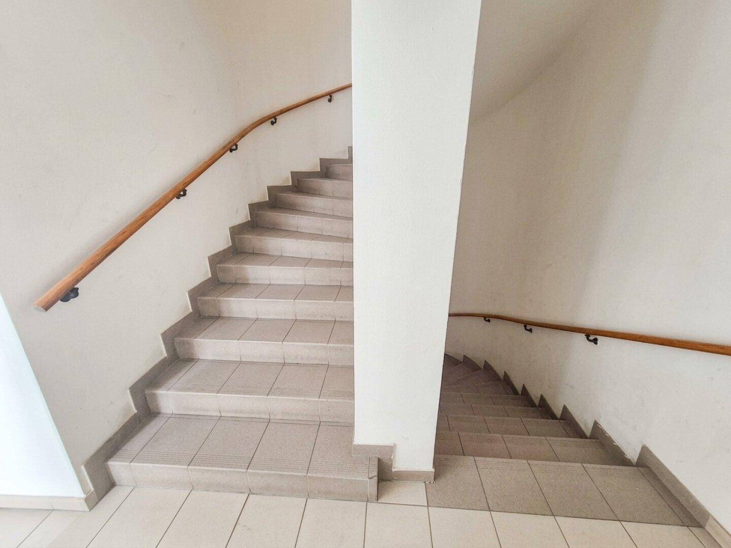 Treppenhaus mit gefliesten Stufen und Holzgeländer, verbindet die verschiedenen Etagen des Gebäudes.
