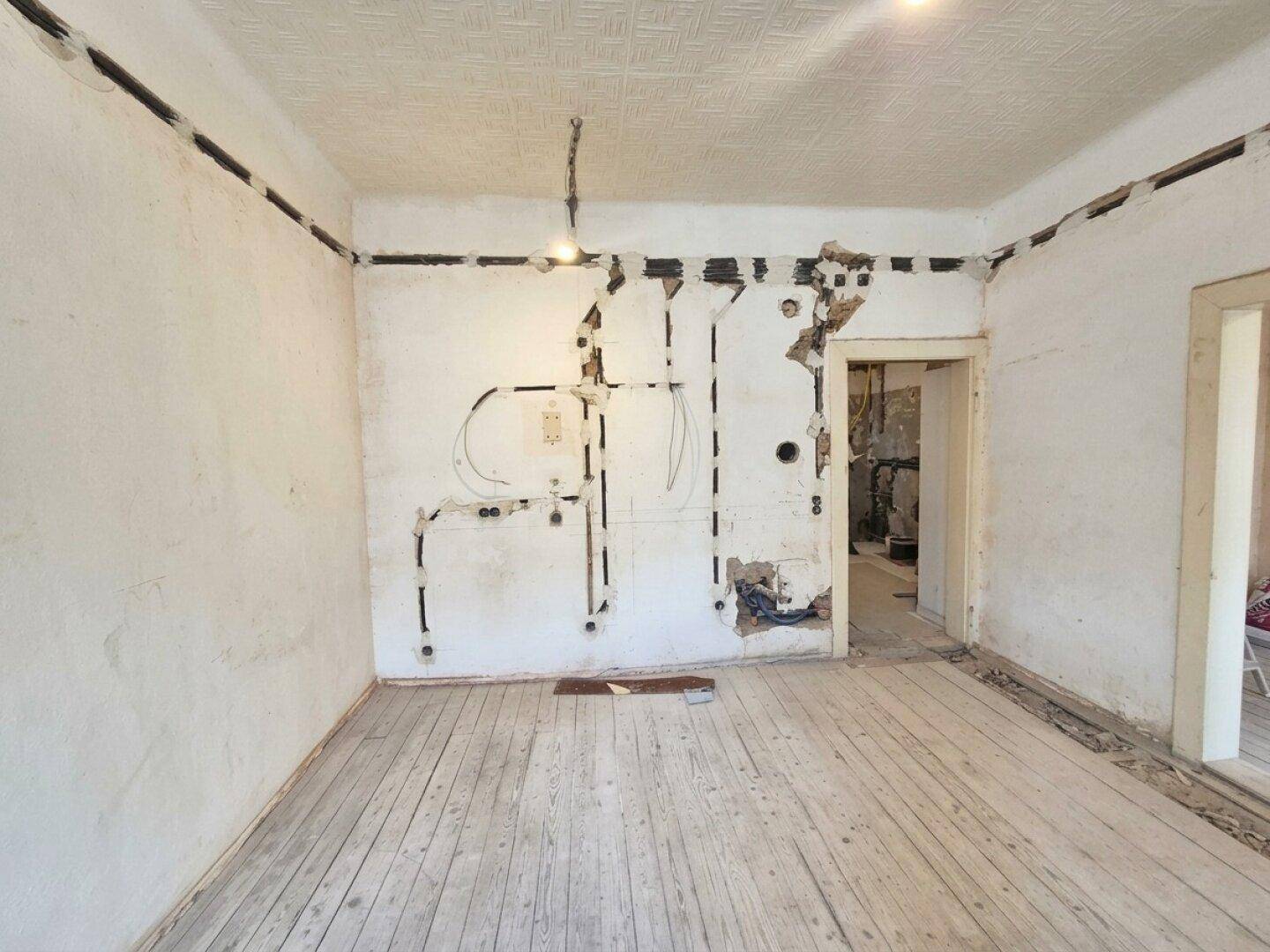 Innenraum im Rohzustand mit sichtbaren Elektroinstallationen und alten Holzdielen, wartet auf Fertigstellung.