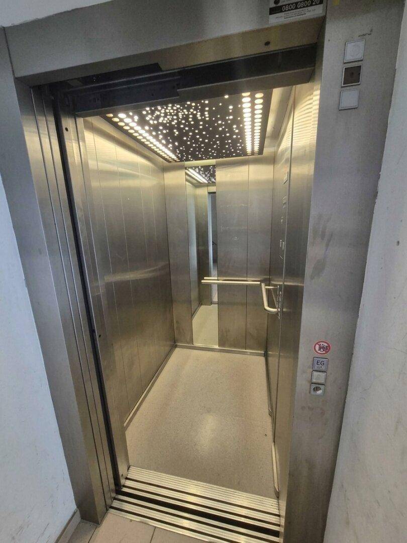 Moderner Aufzug mit Edelstahloberflächen und dekorativer Deckenbeleuchtung im Eingangsbereich.