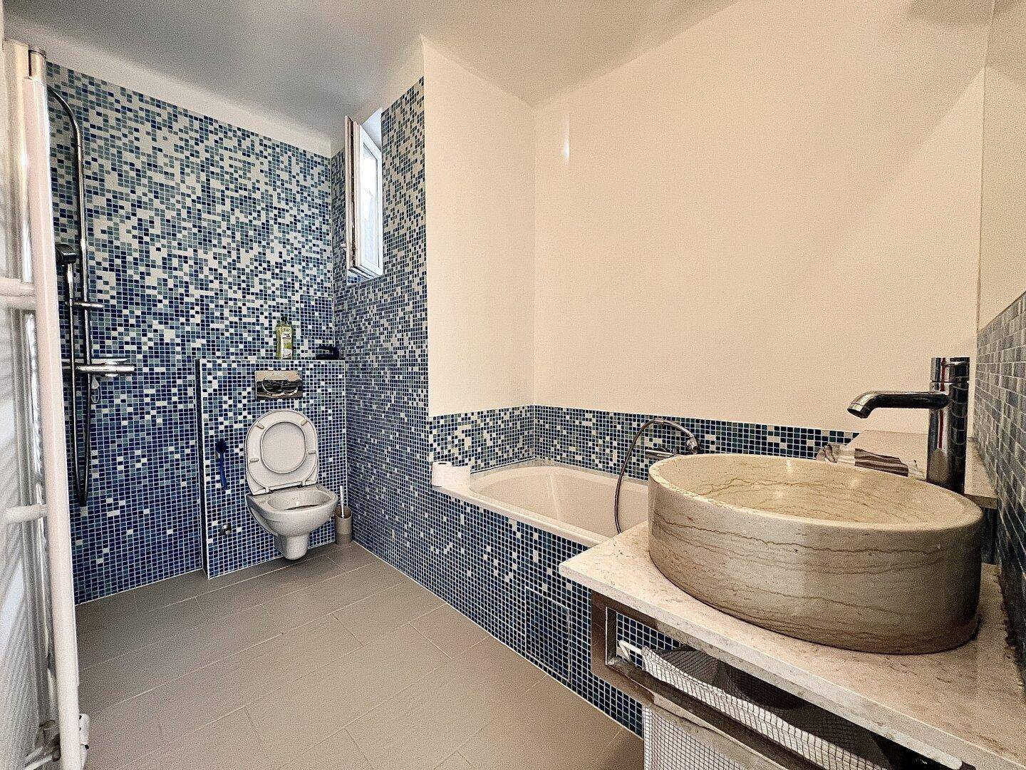 Modernes Badezimmer mit blauen Mosaikfliesen, Badewanne, Dusche und stilvollem Aufsatzwaschbecken.