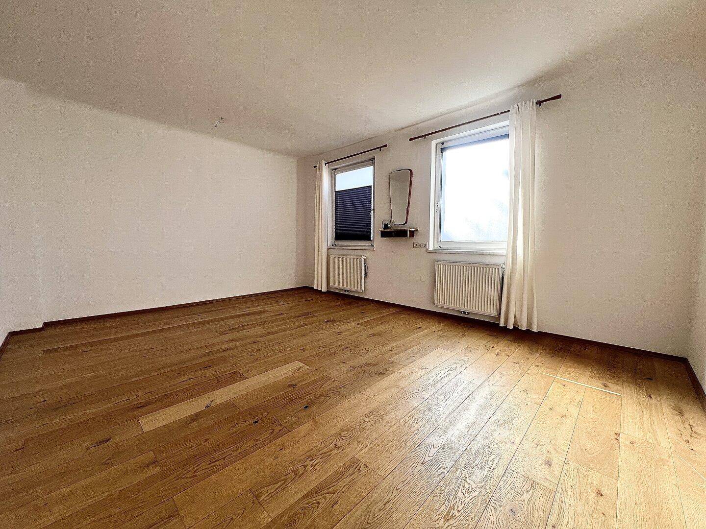 Helles Zimmer mit Holzboden und zwei Fenstern, ideal als Schlaf- oder Arbeitszimmer nutzbar.