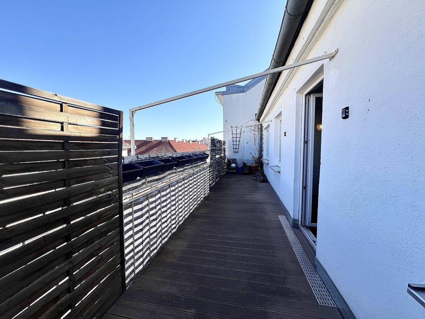 Langer Balkon mit Holzdielen und Sichtschutz, bietet einen Blick über die Dächer der Stadt.