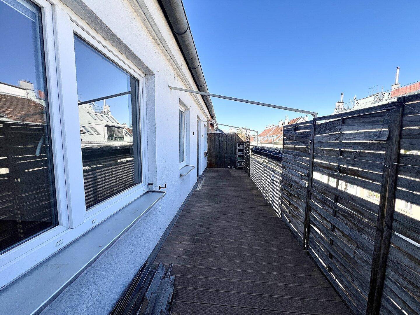 Sonniger Balkon mit Holzboden und seitlichem Sichtschutz, zugänglich von den Innenräumen.