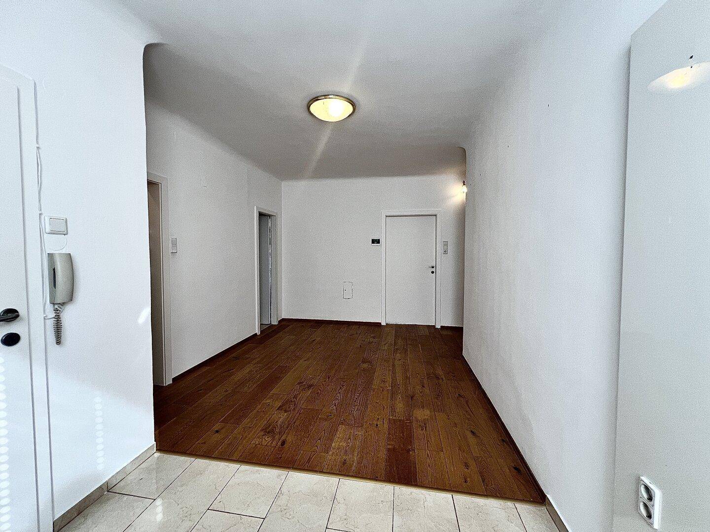 Geräumiger Flur mit Holzboden und Gegensprechanlage, verbindet verschiedene Wohnbereiche.