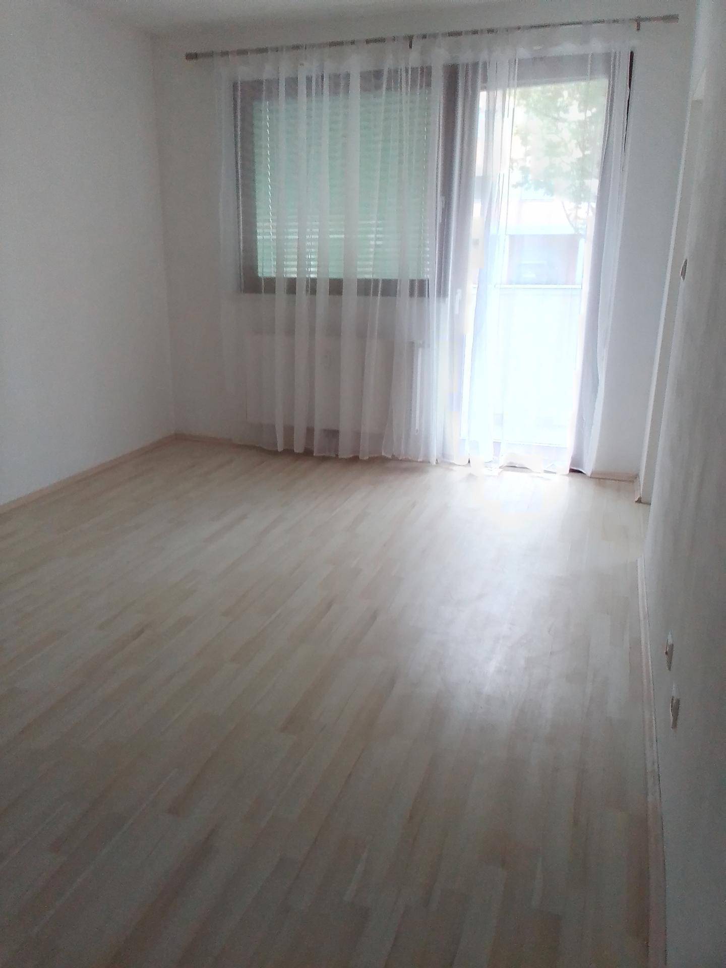 Heller Raum mit hellem Laminatboden und Zugang zu einem Balkon.