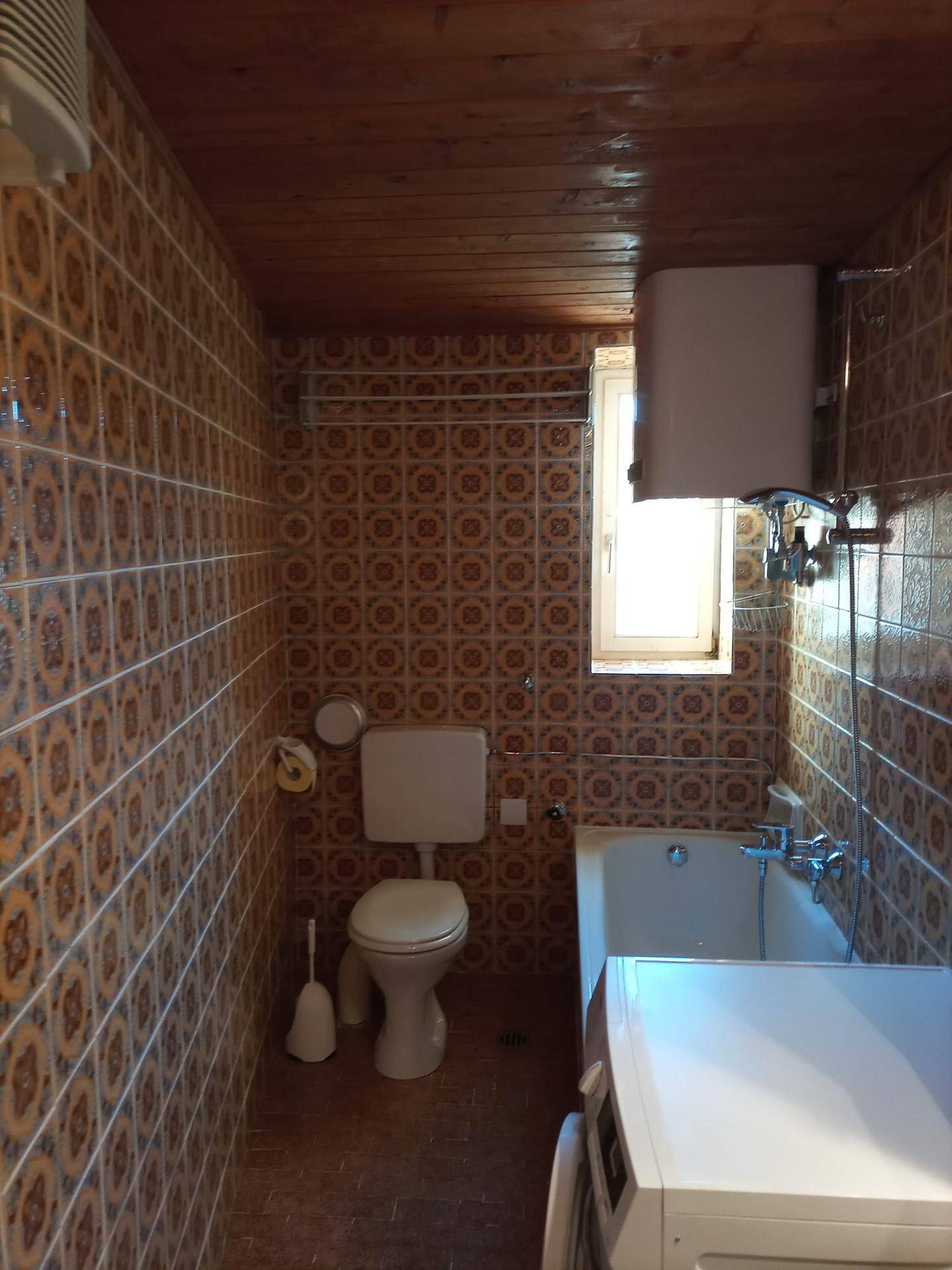 Badezimmer mit Badewanne, Toilette, Waschbecken und Waschmaschine, komplett gefliest.
