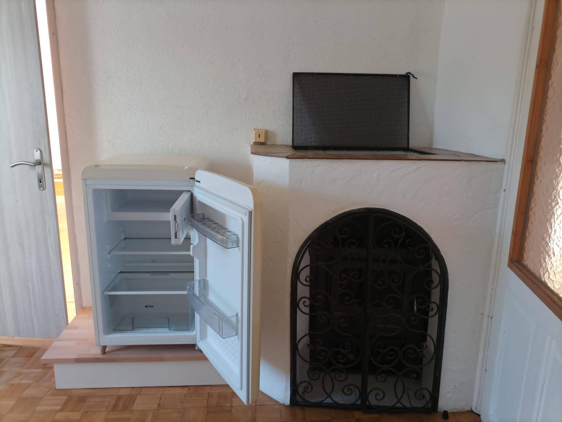 Raum mit Parkettboden, kleinem Kühlschrank und einem dekorativen Kamin-Element.