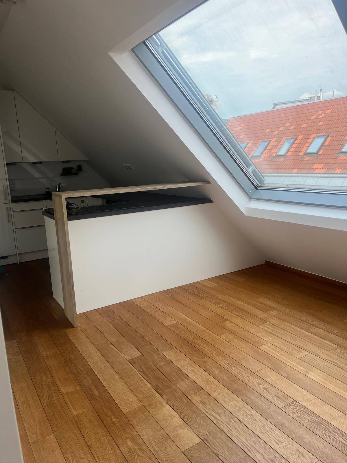 Heller Dachgeschossraum mit Holzboden, großem Dachfenster und Thekenbereich.