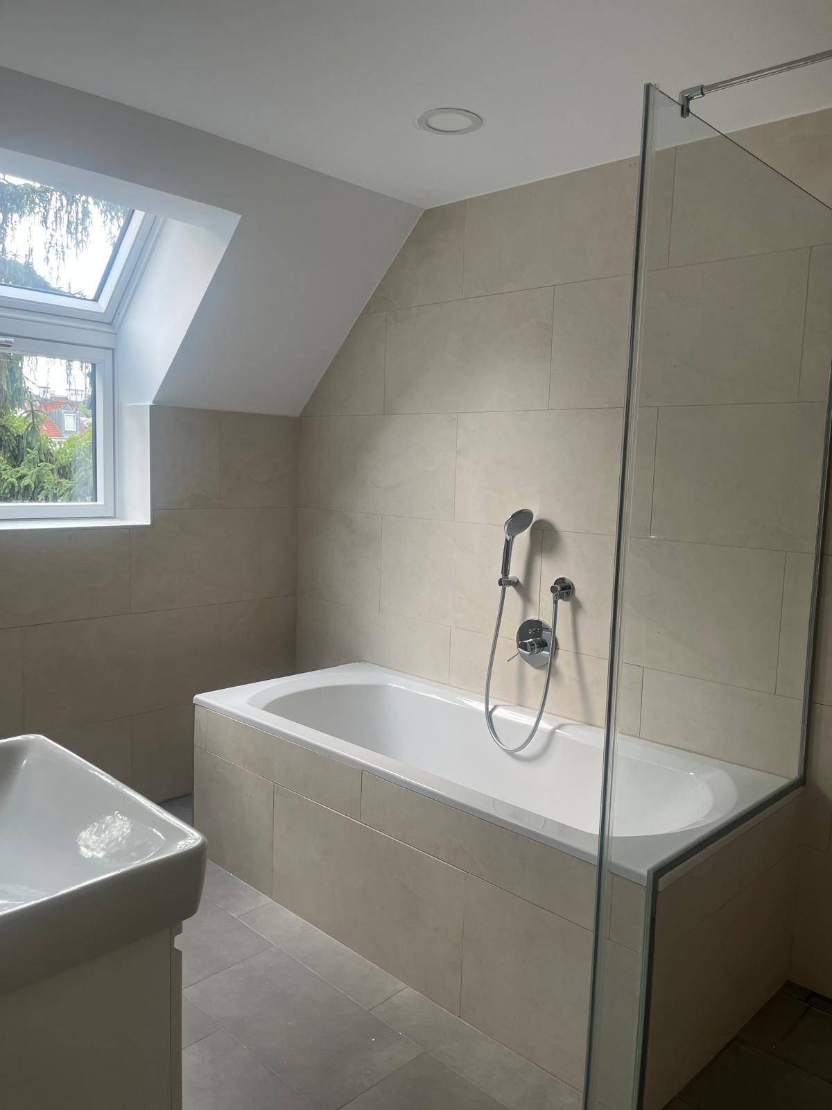Helles Badezimmer mit Badewanne, Duschbereich, Waschbecken und Dachfenster.