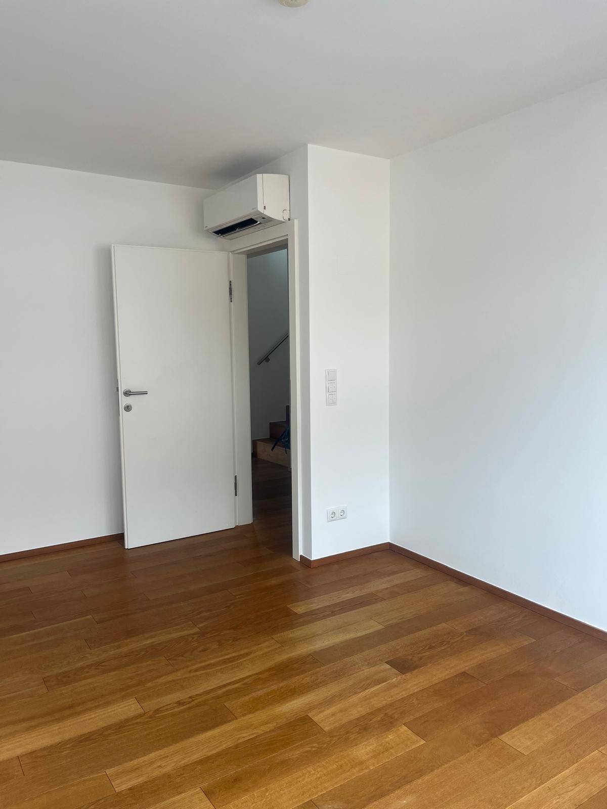 Helles Zimmer mit Holzboden, weißen Wänden und Klimaanlage.