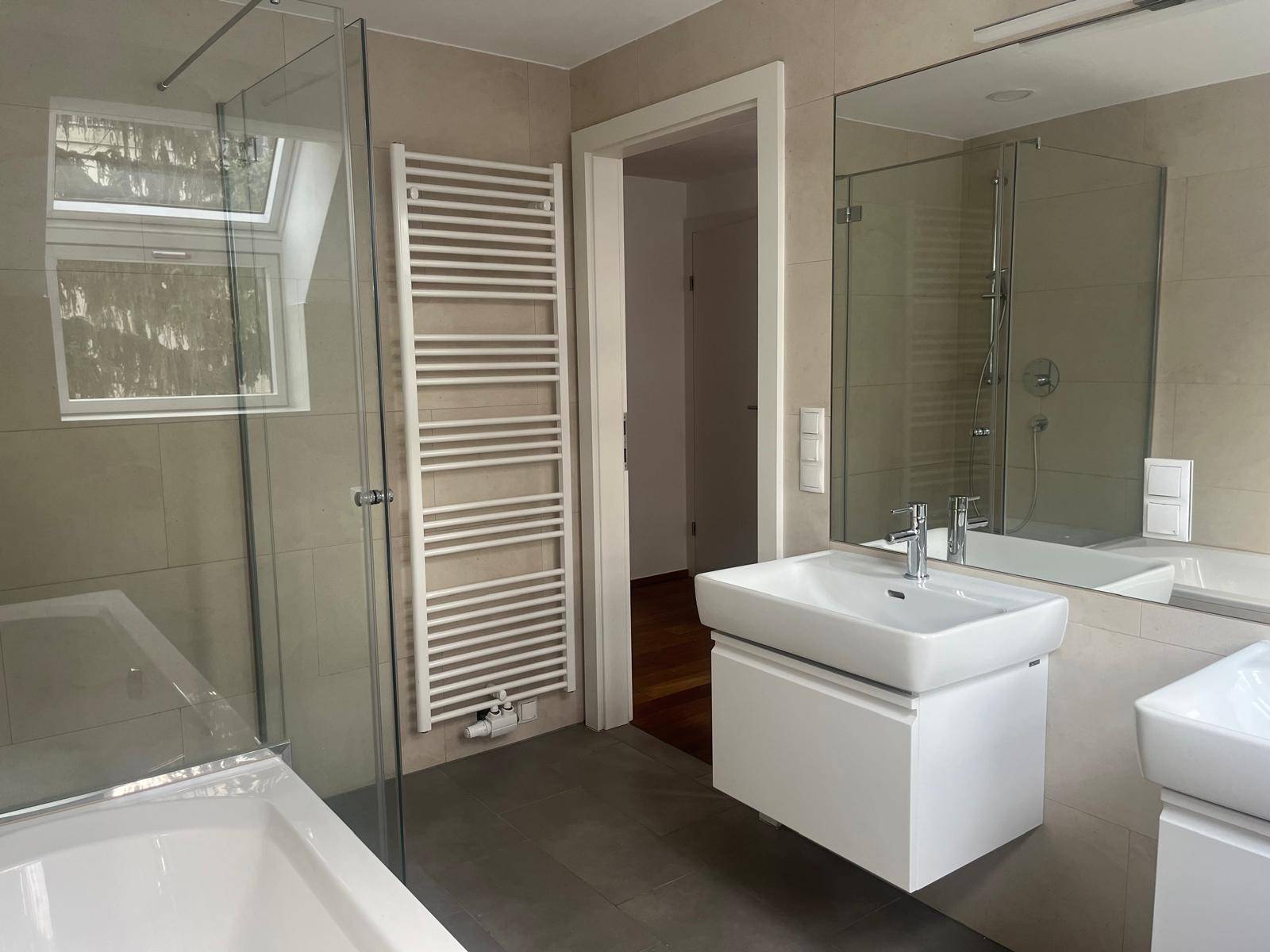 Modernes Badezimmer mit Badewanne, Dusche, Waschbecken, beheiztem Handtuchhalter und Dachfenster.