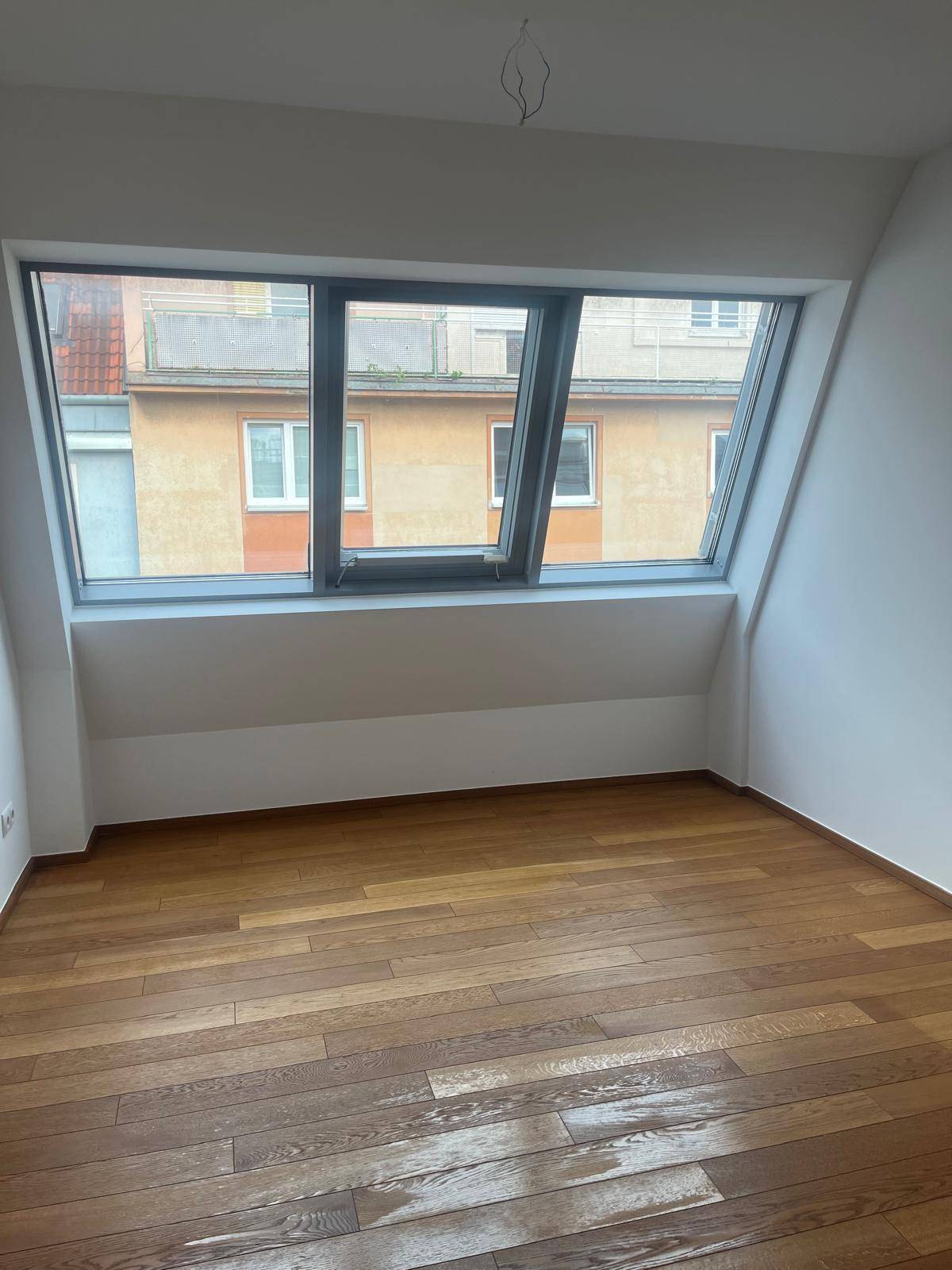 Helles Zimmer mit Holzboden und großem Dachfenster, mit Blick auf die umliegenden Gebäude.