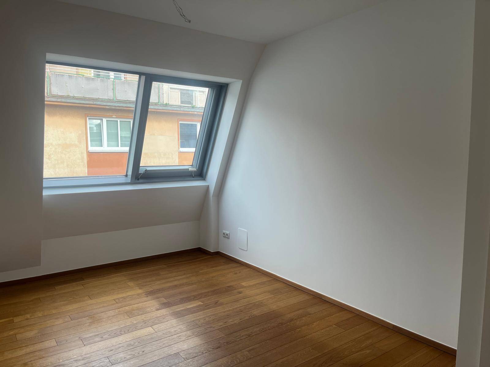 Geräumiges Zimmer mit Holzboden und großem Dachfenster, Blick auf die Stadt.