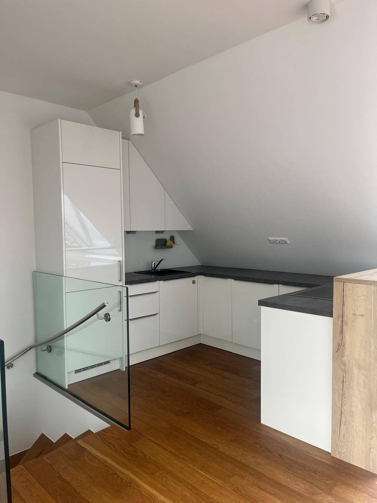 Moderne Küchenzeile im Dachgeschoss mit weißen Schränken, dunkler Arbeitsplatte und Holzboden.