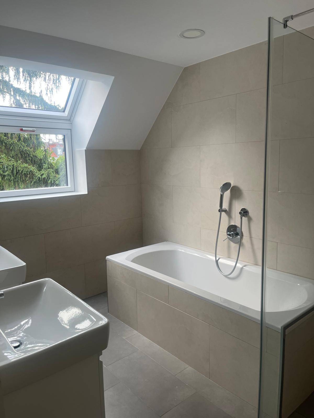 Helles Badezimmer mit Badewanne, Duschbereich, Waschbecken und Dachfenster.