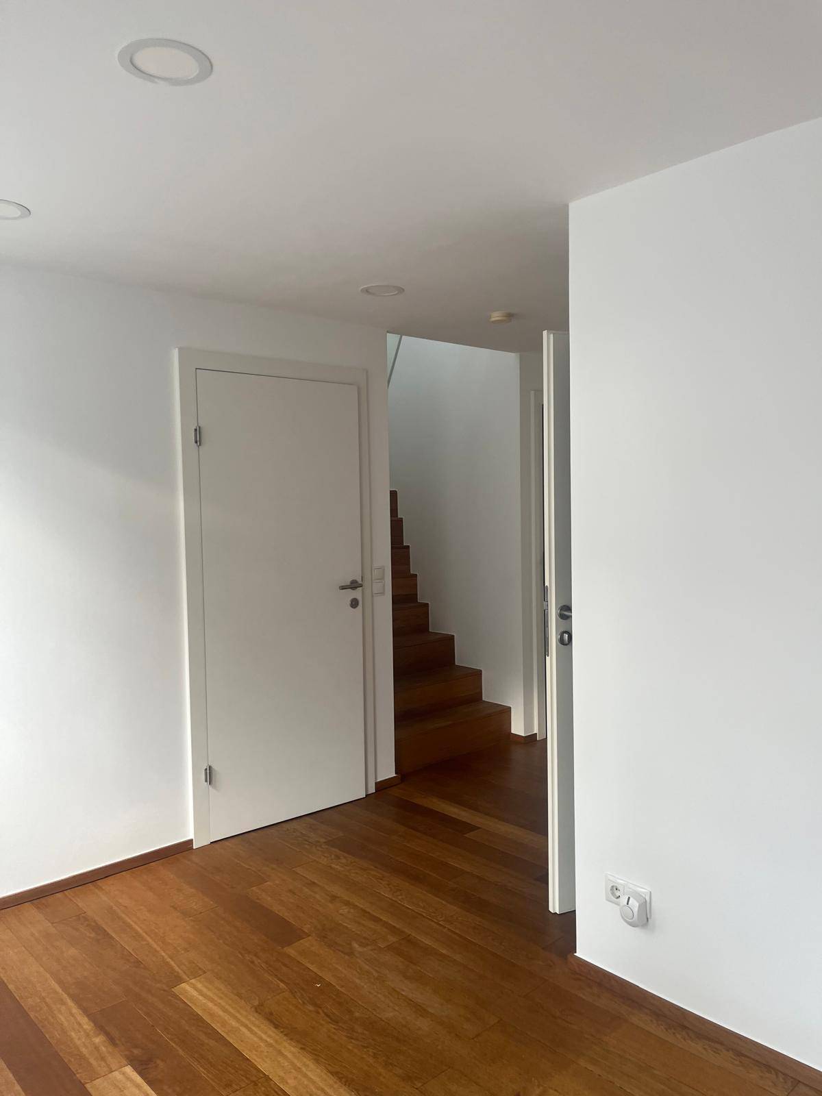 Heller Raum mit Holzboden und weißen Wänden, mit Zugang zur Treppe.
